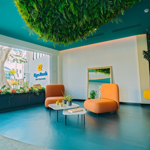 Lobby de 001 Hotels: Corporativa con sillones naranjas, espejo y vegetación colgante.