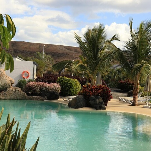 Piscina turquesa con palmeras, tumbonas y paisaje árido, ideal para 001 Hotels Corporativa.
