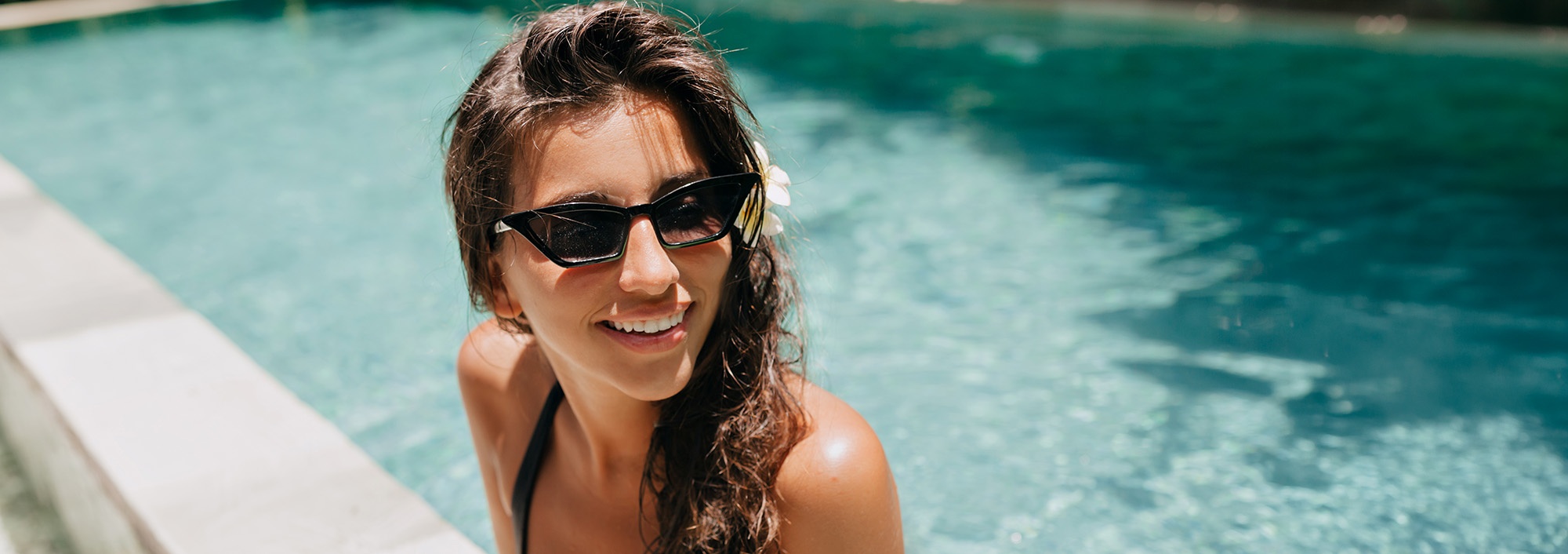 Mujer sonriente con gafas de sol en piscina, ideal para 001 Hoteles Corporativos.