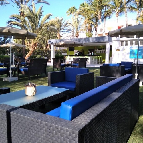 Espacio exterior de 001 Hotels Corporativa: área de descanso con sofás y mesas bajo palmeras.