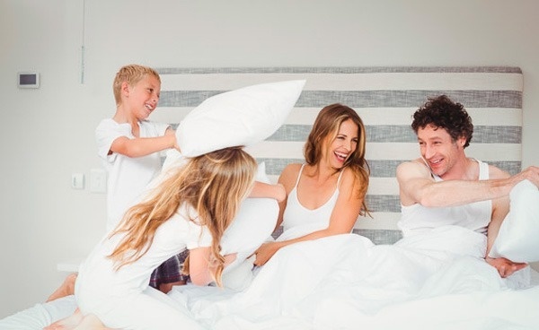 a family is having a pillow fight in bed .