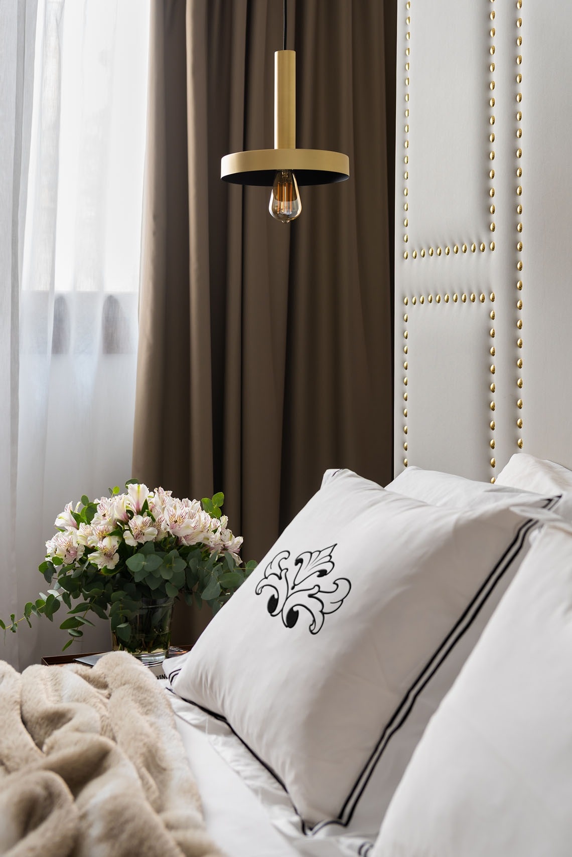 una cama con una almohada bordada y un jarrón de flores