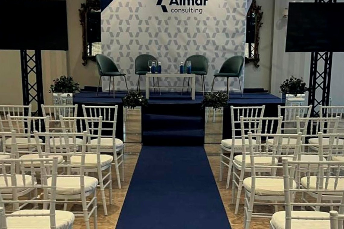 un auditorio con sillas blancas y una alfombra azul y un cartel que dice ' aimar consulting '