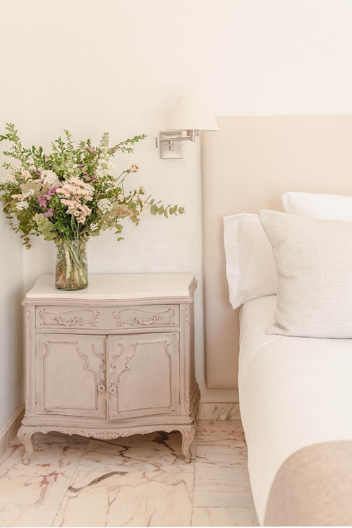 a vase of flowers sits on a nightstand next to a bed