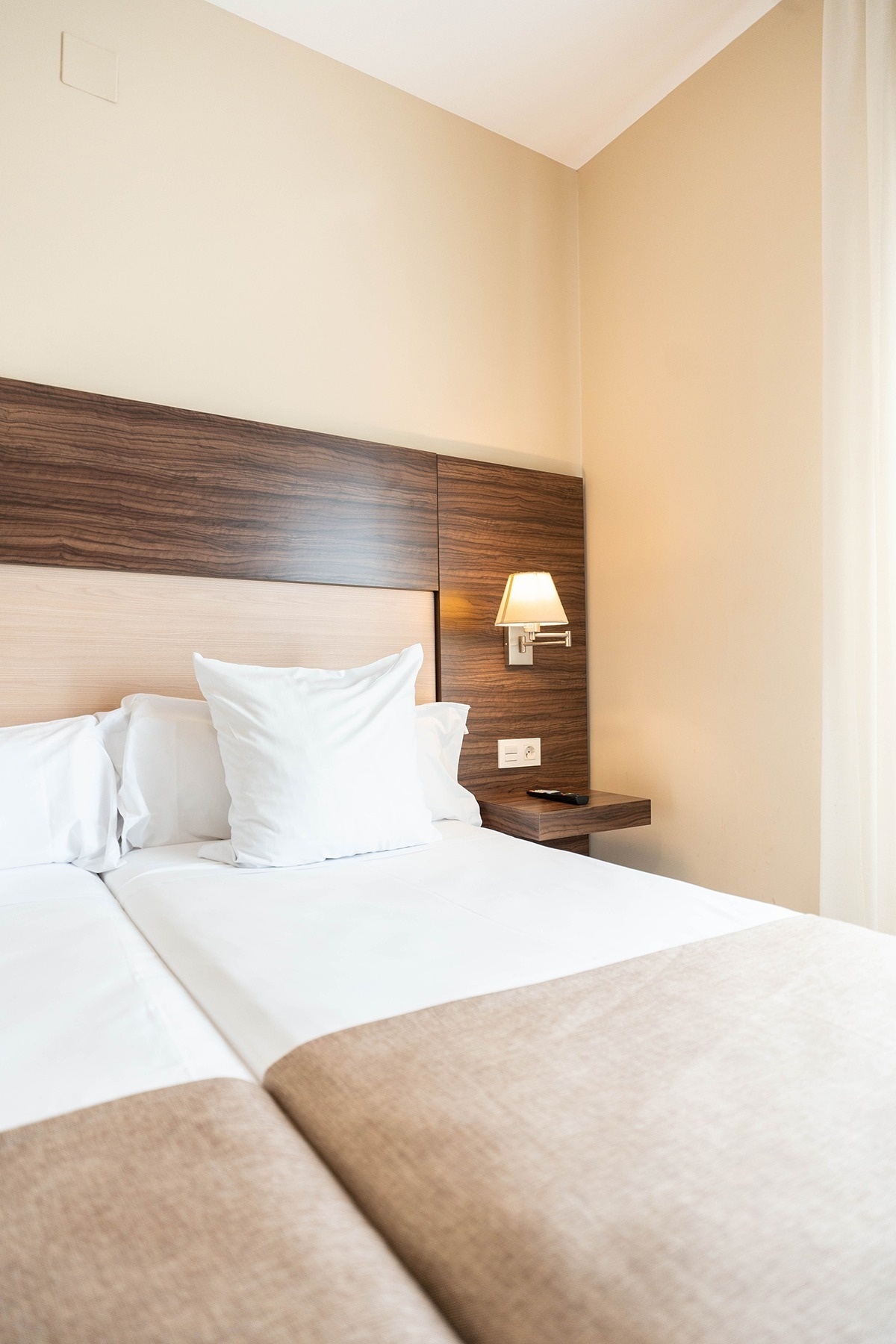 a hotel room with two beds and a lamp on the wall