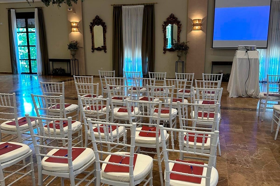 rows of white chairs with red cushions in front of a projector screen
