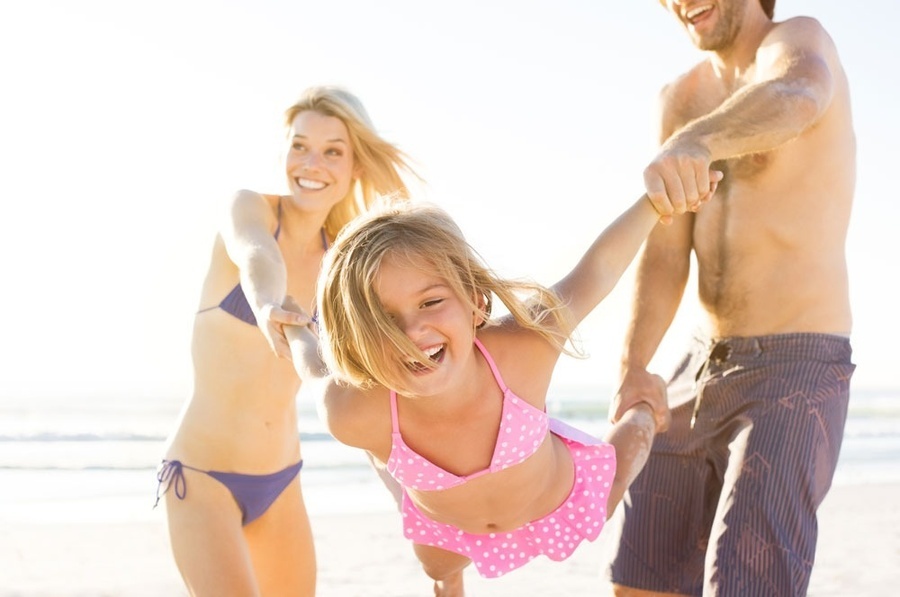 un hombre y una mujer sostienen a una niña en el aire en la playa