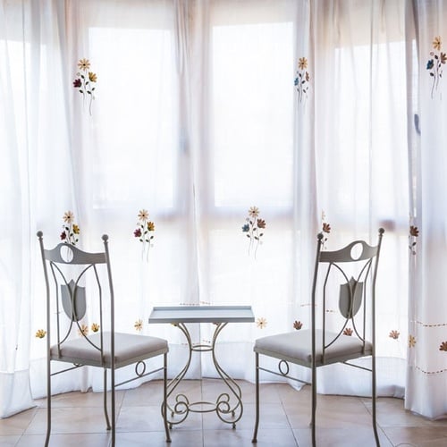 Two vintage chairs and table before a window with curtains, Torre Cristina Hotel.