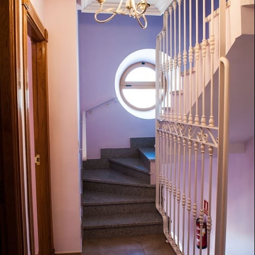 Torre Cristina interior staircase with wooden door, round window, and white railing.