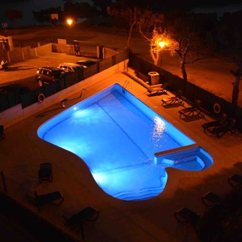Torre Cristina's illuminated pool at night, featuring lounge chairs and trees.