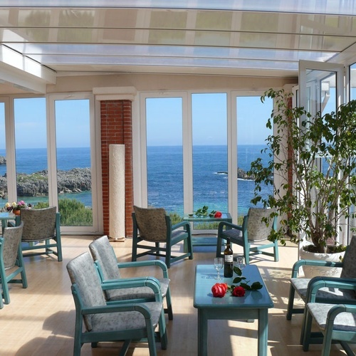 Glass-enclosed terrace at Torre Cristina with sea views and armchairs.