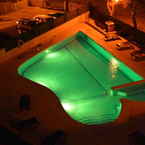 Torre Cristina's illuminated pool at night, with lounge chairs and parked cars.