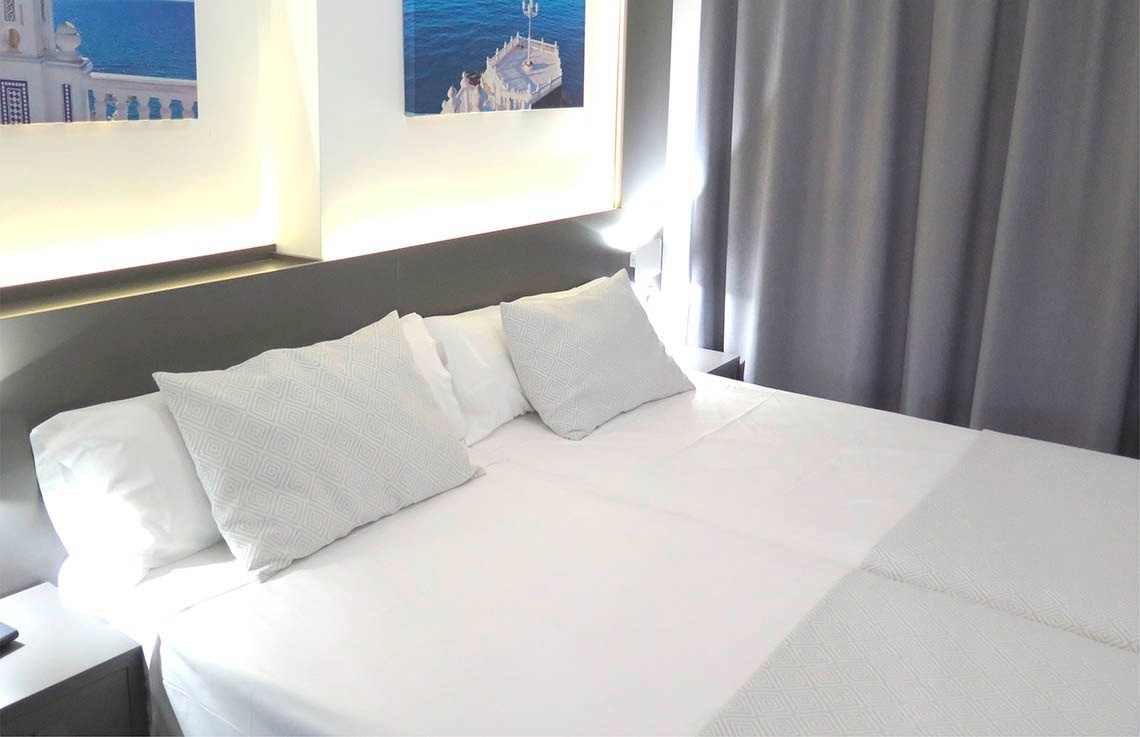 a bed with white sheets and pillows in a hotel room