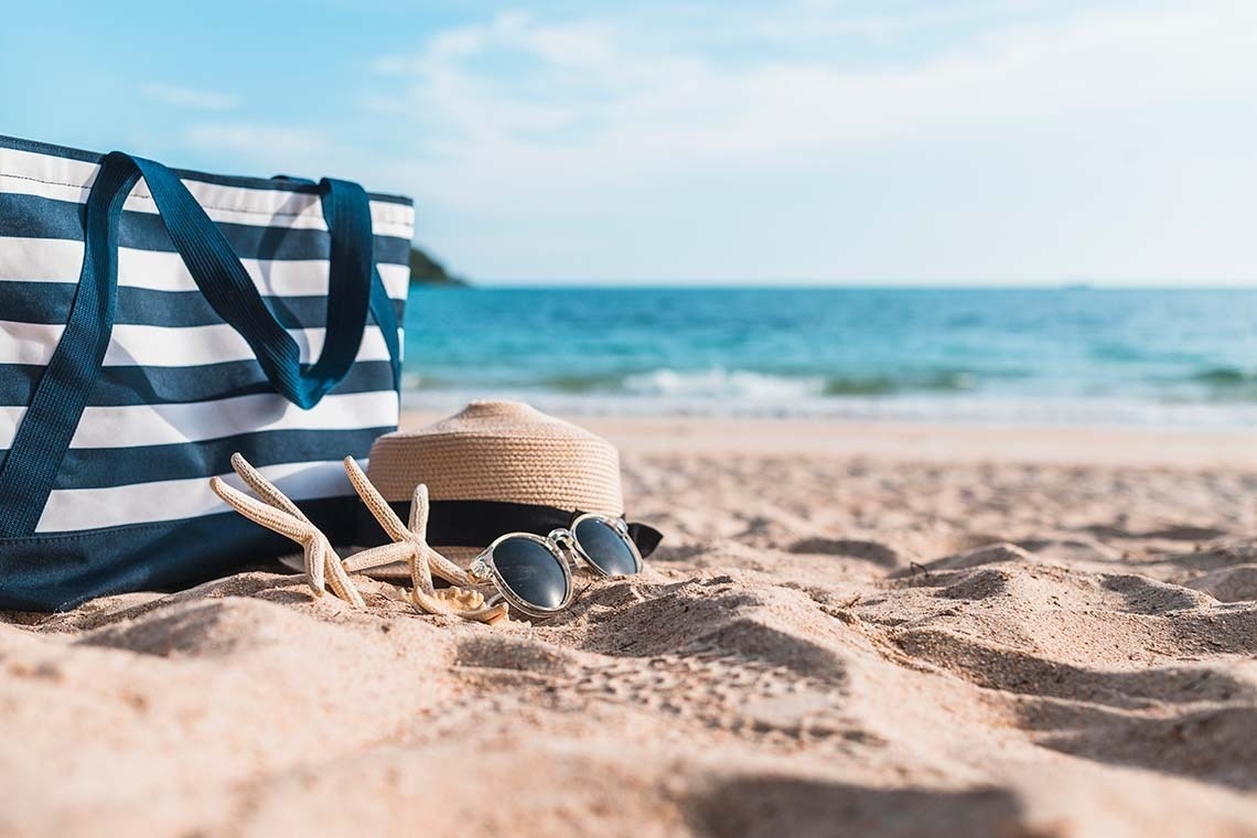 una bolsa de playa a rayas con un sombrero y gafas de sol en la arena