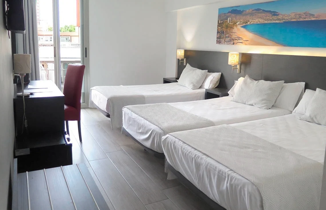 a hotel room with three beds and a picture of a beach on the wall