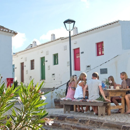 a group of people sit at a table in front of a white building with a red door