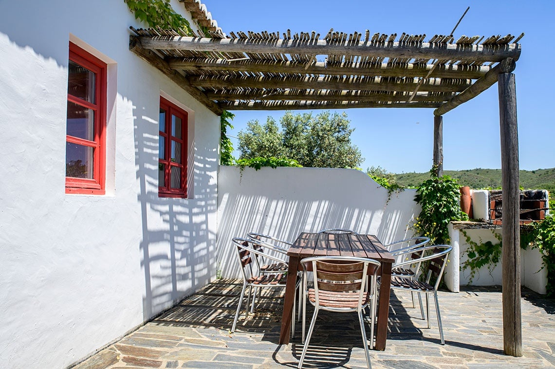 Pátio de Aldeia da Pedralva com mesa e cadeiras sob um telhado de palha.