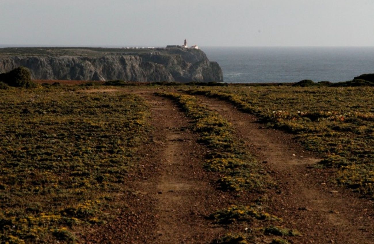 uma estrada de terra com um farol ao fundo