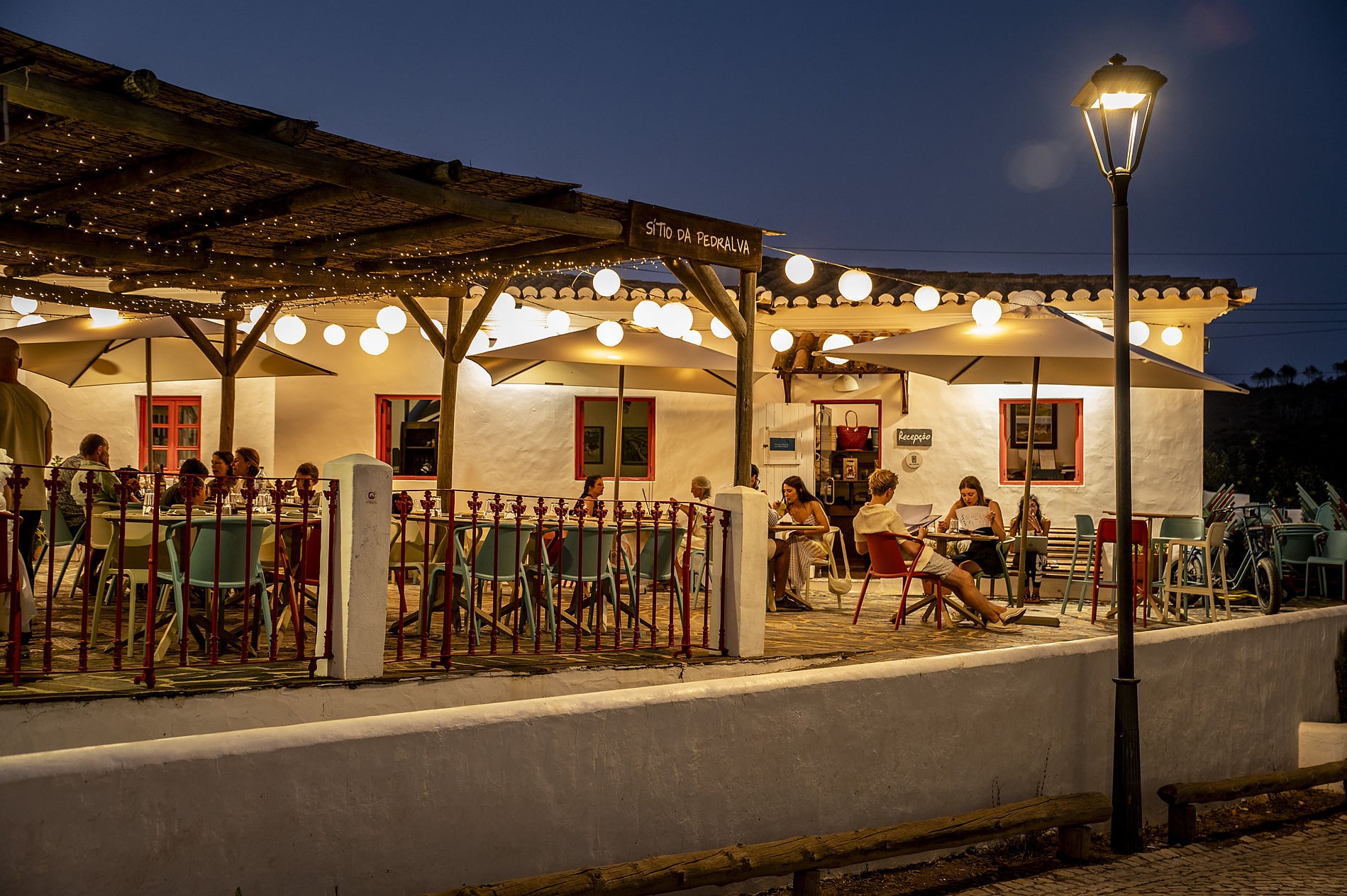 Restaurante ao ar livre na Aldeia da Pedralva, com pátio de pedra, edifícios brancos e esplanada.