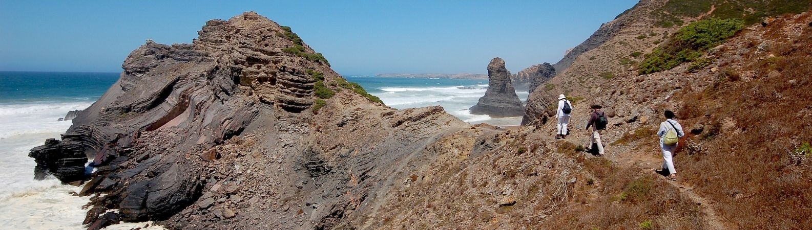 um grupo de pessoas caminha por uma trilha ao lado de um penhasco com vista para o oceano