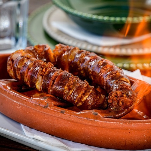 two sausages in a clay dish with flames in the background
