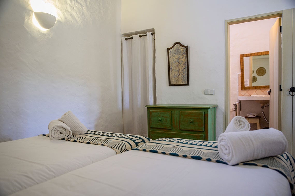 Duplo quarto na Aldeia da Pedralva com roupa de cama branca e toalhas enroladas.