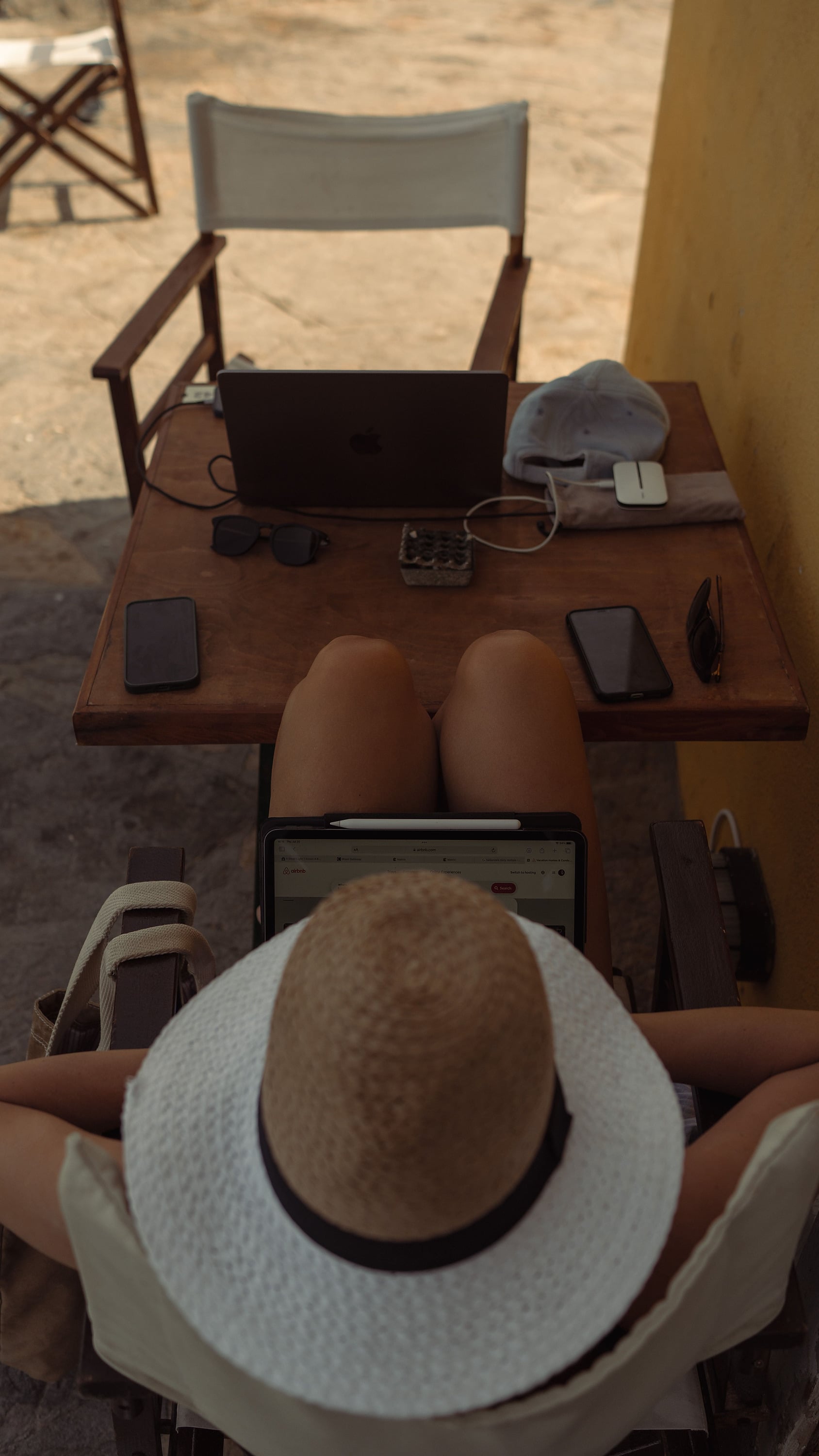 Mulher relaxa em cadeira de praia com laptop, tablet e celular, pronta para planejar sua Aldeia da Pedralva.