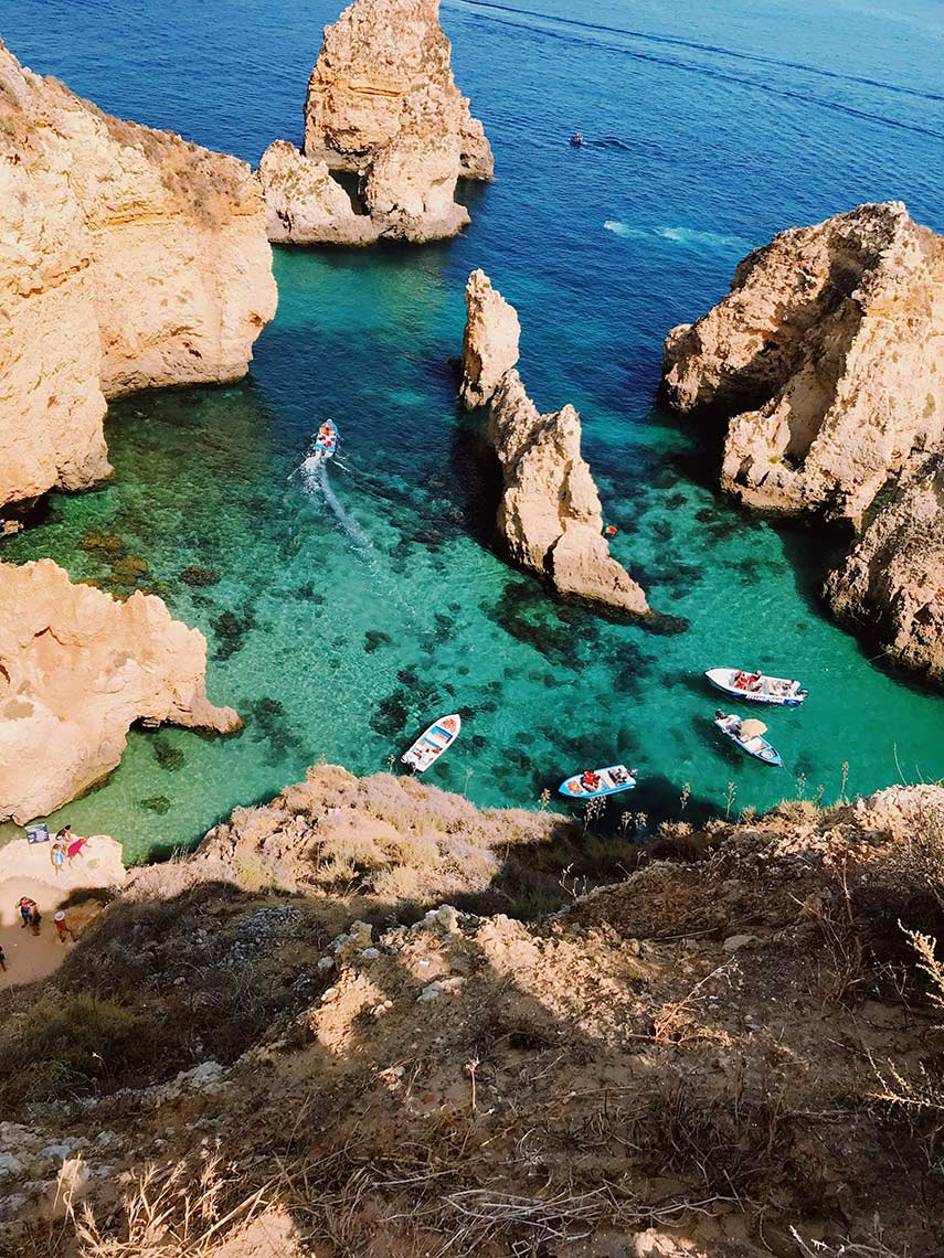 Clear turquoise waters with boats near Aldeia da Pedralva hotel and cliffs.