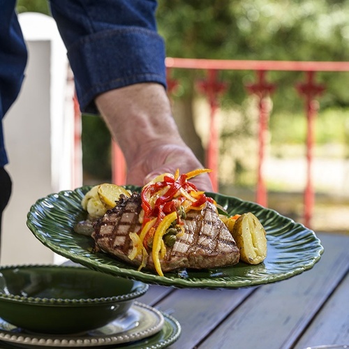 a person is holding a plate of grilled meat and vegetables