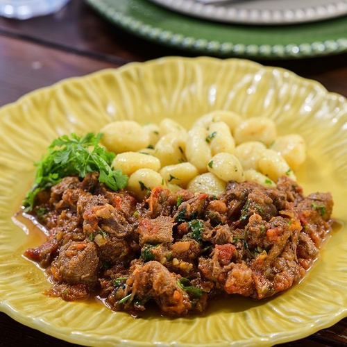 a yellow plate with meat and gnocchi on it