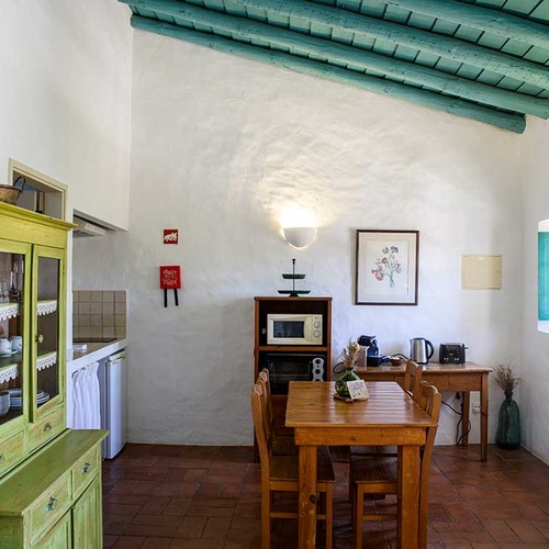 Cozy kitchen and dining area at Aldeia da Pedralva with rustic green cabinet and wooden table.