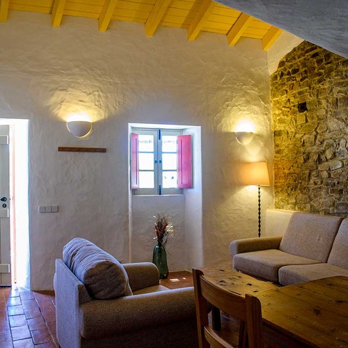 Cozy living room at Aldeia da Pedralva with stone walls, rustic furniture, and yellow ceiling beams.