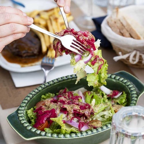 A fork lifts a salad with red cabbage, lettuce, and dressing from a green bowl at Aldeia da Pedralva.