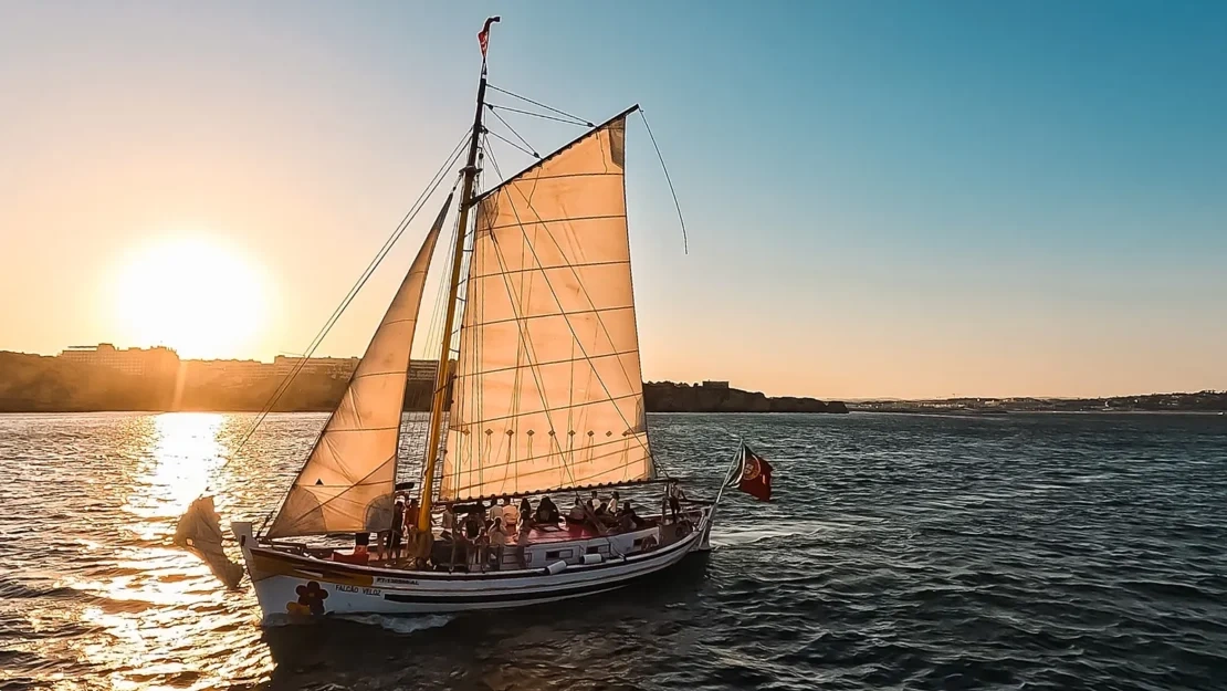 um barco com as velas abaixadas está flutuando no oceano ao pôr do sol