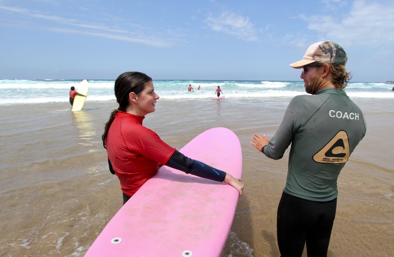 un hombre con la camisa coach sostiene una tabla de surf rosa