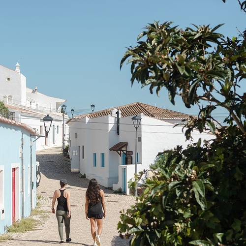 dos mujeres caminan por una calle de ladrillos junto a edificios blancos