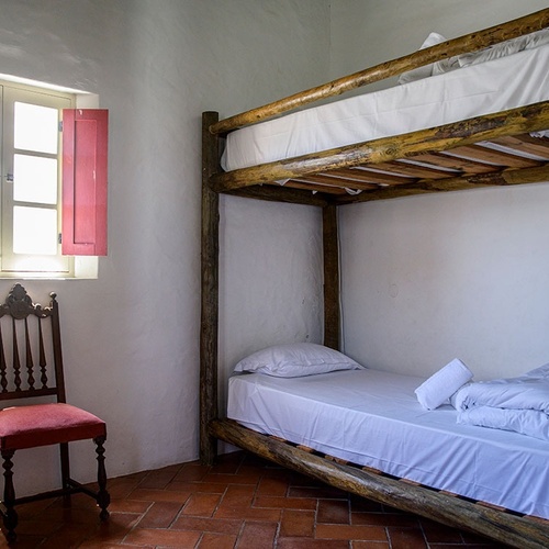 a bunk bed with white sheets and a red chair in front of it