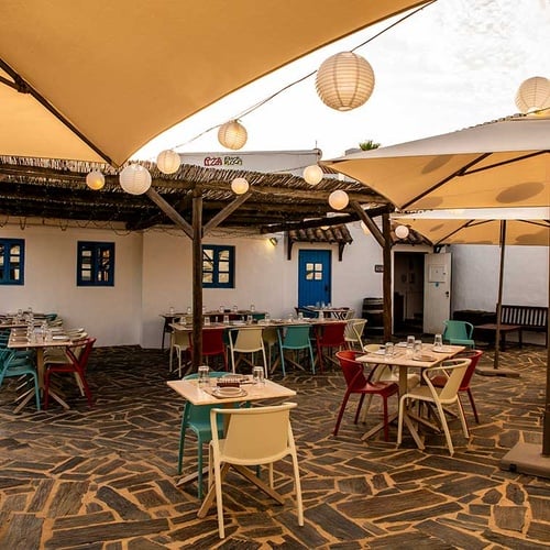 Charming outdoor dining area at Aldeia da Pedralva, with tables set under a thatched roof and umbrellas.