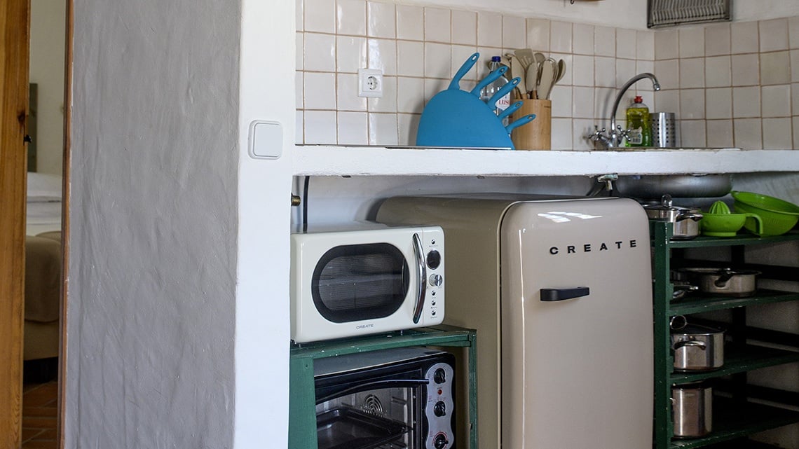 Cozinha charmosa na Aldeia da Pedralva com micro-ondas, frigorífico retrô e utensílios.