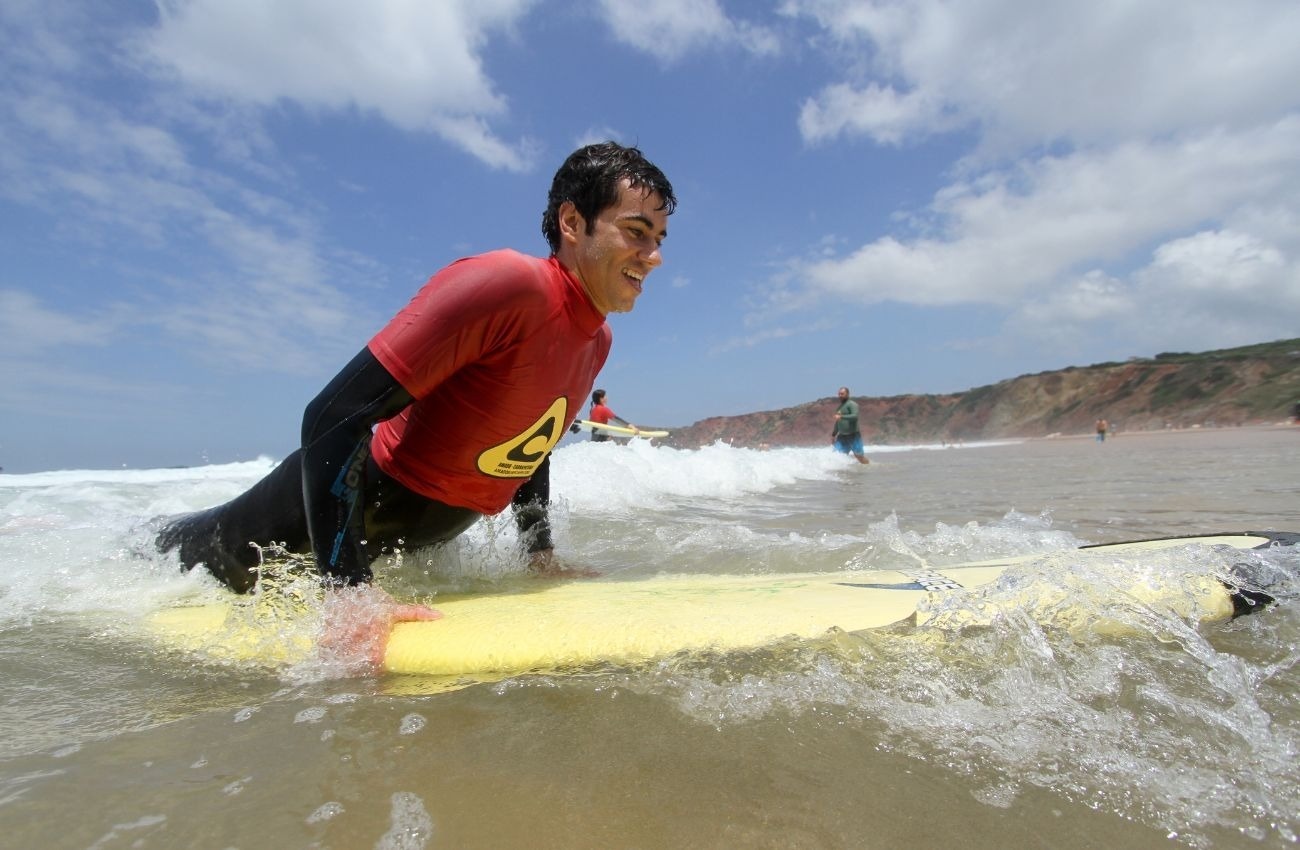 um homem em uma camisa vermelha com a letra a em amarelo está deitado em uma prancha de surf