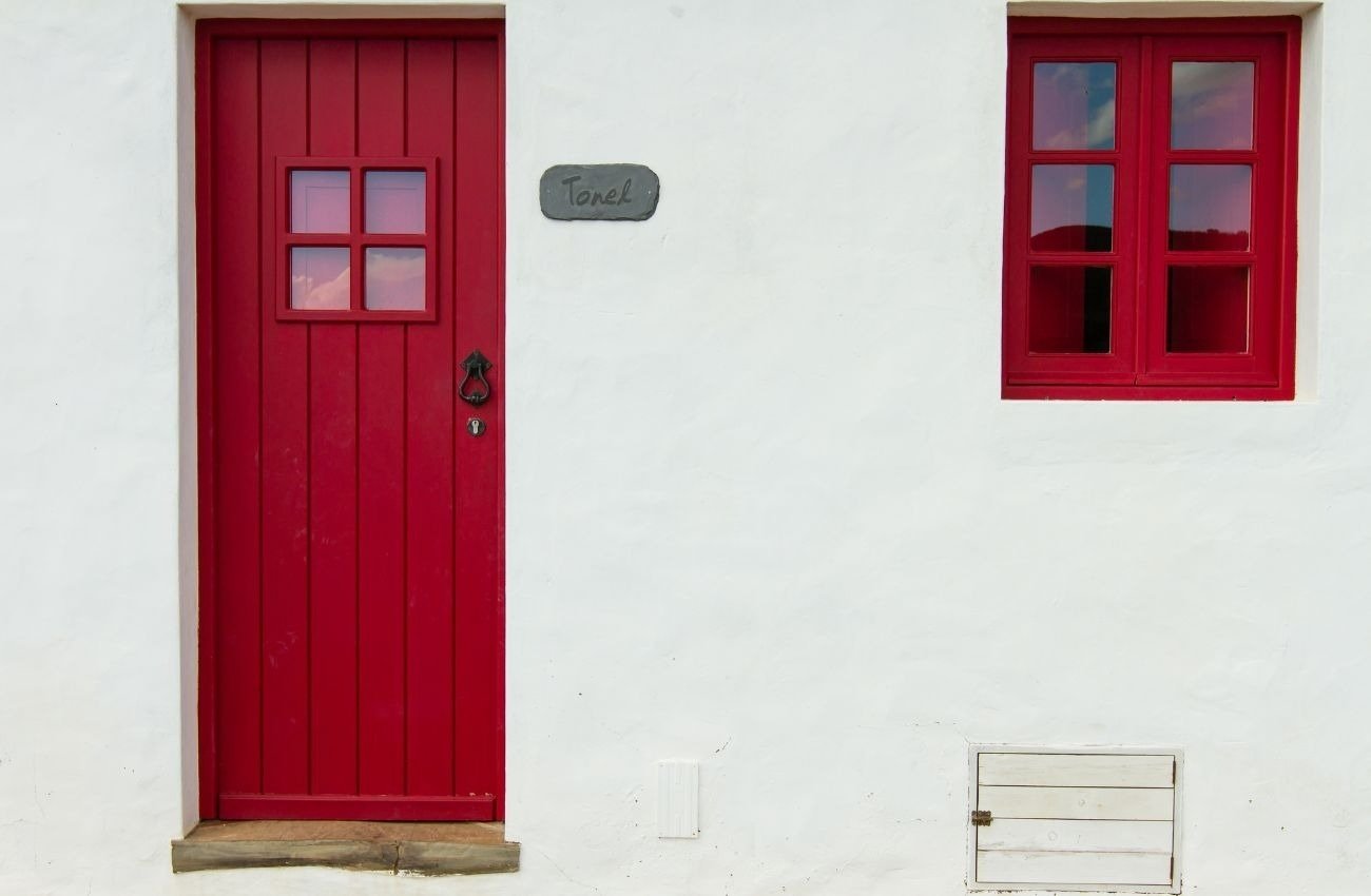 uma porta vermelha e duas janelas vermelhas em uma parede branca