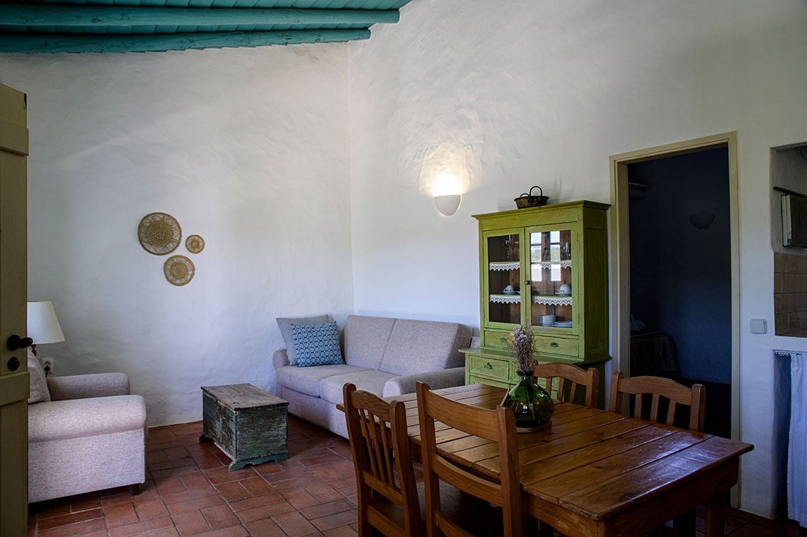 Sala de estar e jantar rústica na Aldeia da Pedralva com sofá, mesa e armário verde.