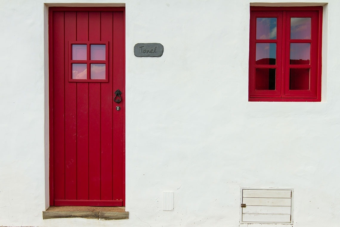 una puerta roja y dos ventanas rojas en una pared blanca