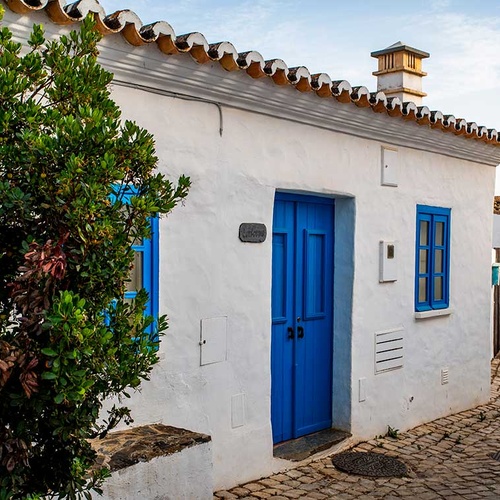 Charming white cottage with blue doors and windows at Aldeia da Pedralva, Portugal.