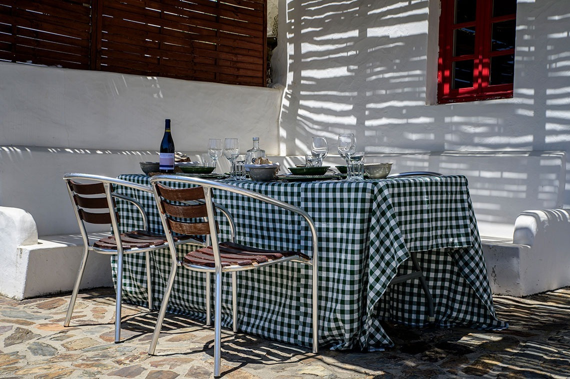 Mesa de jantar exterior rústica em Aldeia da Pedralva, com toalha xadrez e vinho, perfeita para refeições ao ar livre.