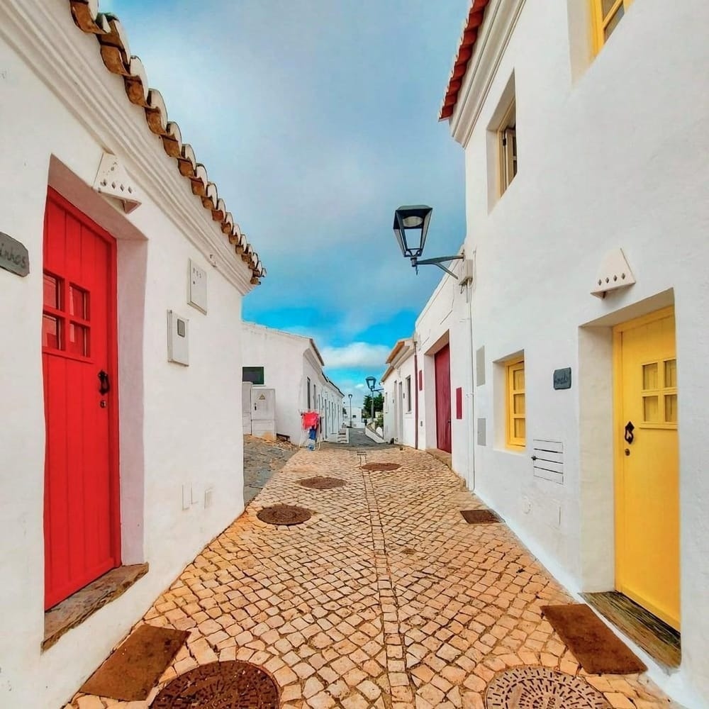 Charming Aldeia da Pedralva street with colorful doors and cobblestones.