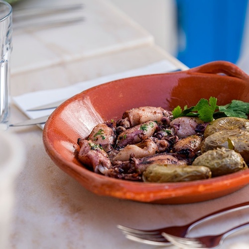 a bowl of food with potatoes and octopus on a table