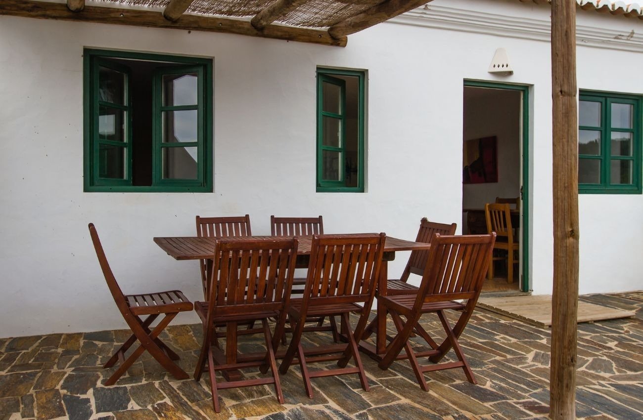 uma mesa de madeira e cadeiras estão em frente a uma casa branca