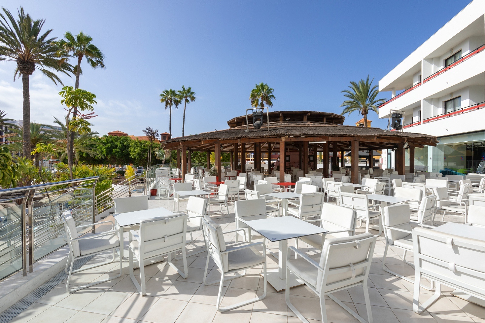 Terraza Alexandre La Siesta Hotel 4 estrellas Tenerife: mesas y sillas blancas bajo palmeras.