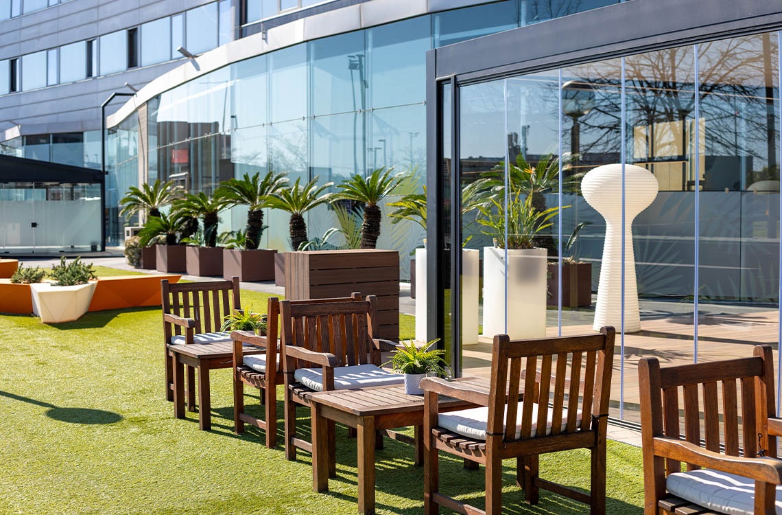 Moderna terraza exterior del Hotel Alexandre Corporativa con césped, mobiliario y restaurante.